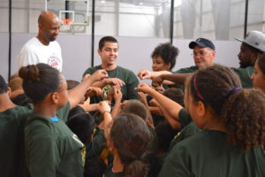 A Terry Scholar stands next to a male coach, leading a team of kids, all placing their hand together in a large circle.