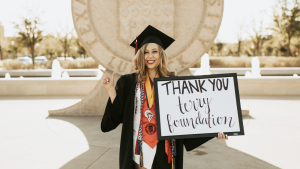 a Terry Scholar in graduation gear holding a sign that says thank you Terry Foundation